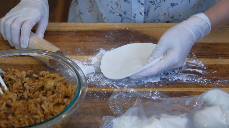 Image of Flatten a small dough into a round patty. Then roll it with a rolling pin. Left hand holds and rotates the dough. Right hand pushes the rolling pin back and forth. Repeat that until you get a big dumpling wrapper, about...