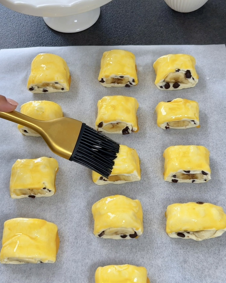 Image of Posmaruj kawałki ciasta ubitym żółtkiem. Piecz w nagrzanym piekarniku w temperaturze 200°C przez około 15-20 minut, aż będą złociste i chrupiące.