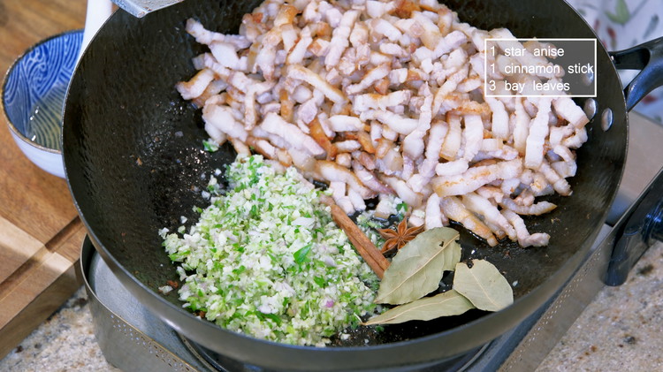 Image of Add the chopped aromatics to the wok along with 1 star anise, 1 cinnamon stick, and 3 bay leaves. Turn the heat back to medium and stir until the aromatics are fragrant.