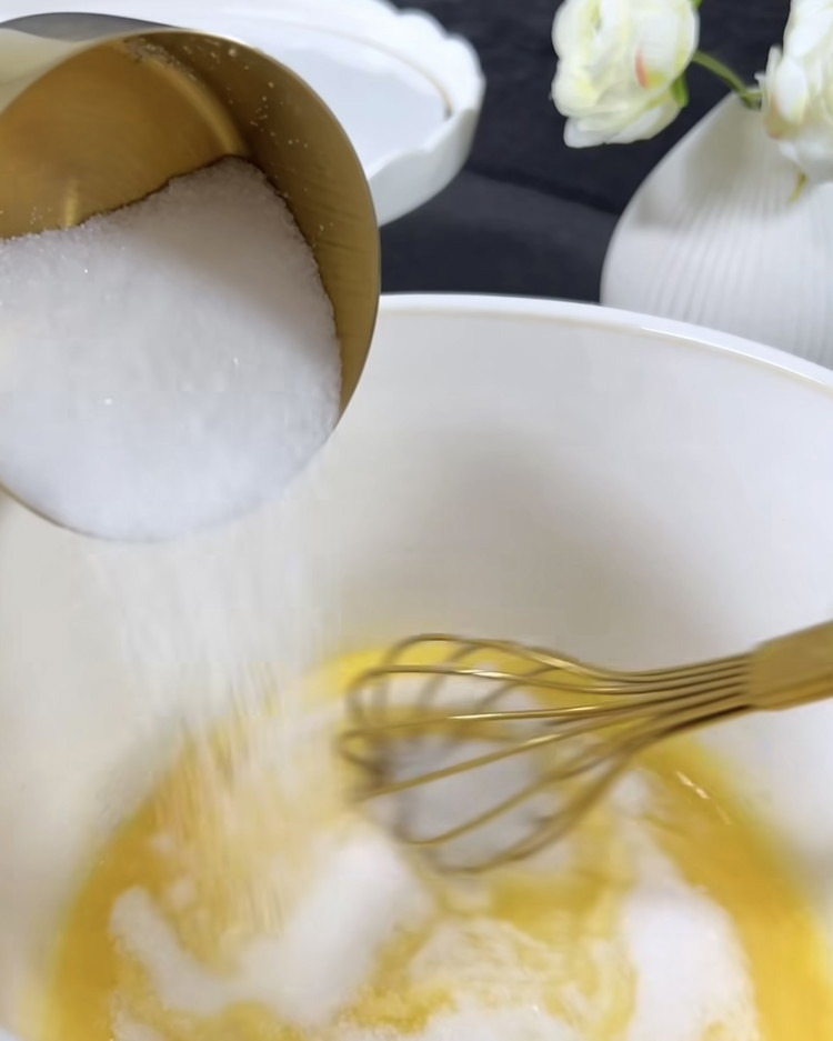 Image of Dans un grand bol, battez le sucre et l'œuf avec un batteur électrique jusqu'à obtenir une consistance mousseuse. Ajoutez l'huile végétale, l'extrait de vanille, le jus de citron et le zeste de citron, puis mélangez bien.