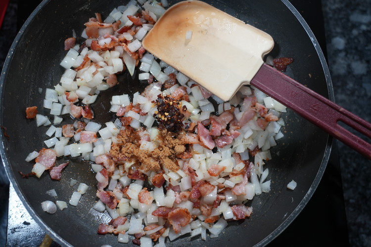 Image of Once the bacon start to brown and crisp up add the diced onions and sauté then add the red pepper flakes and ½ of the dark brown sugar. 