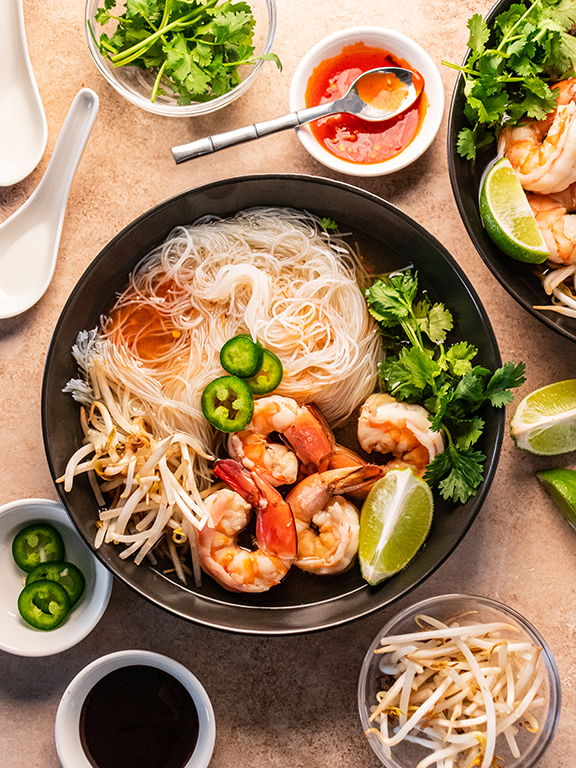 Image of Top with bean sprouts, jalapeño slices, cilantro, lime wedges, hoisin...