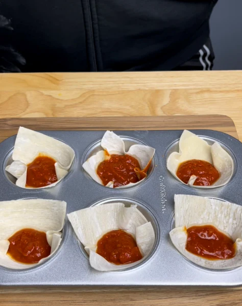 Image of Place one wonton shell into each muffin ring. Add a layer of sauce