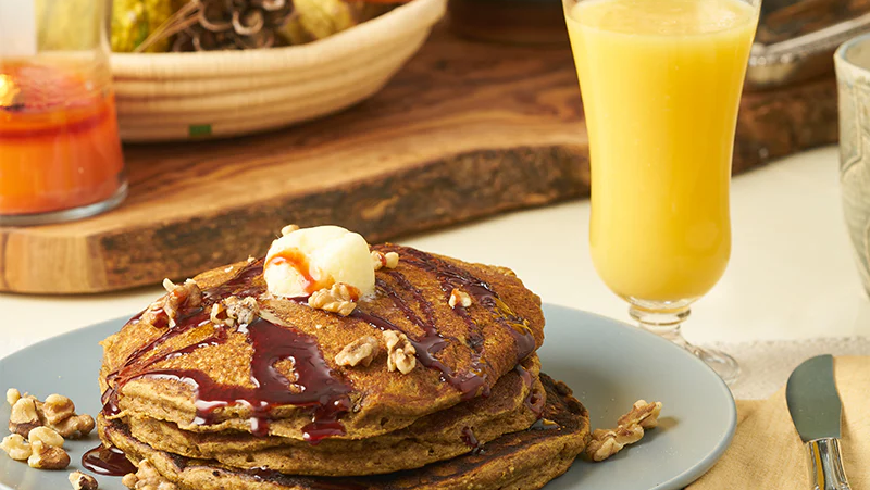 A platter of three pancakes made with purdate date sugar. Glass of orange juice.