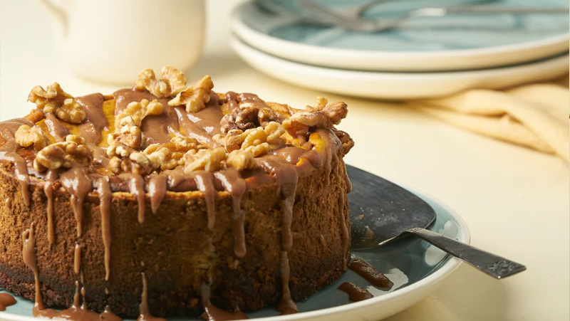 Pumpkin cheesecake topped with walnuts on a plate. A pitcher and two plates set aside.