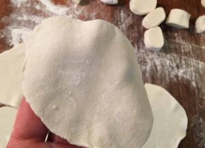 Image of Prosegui con l'impasto: tira fuori la palla con l'impasto dal sacchetto. Faremo le tasche di pasta con questo. Taglia la palla a metà e metti da parte una metà. Stendi l'altra metà in un rotolo di pasta lungo circa 30...