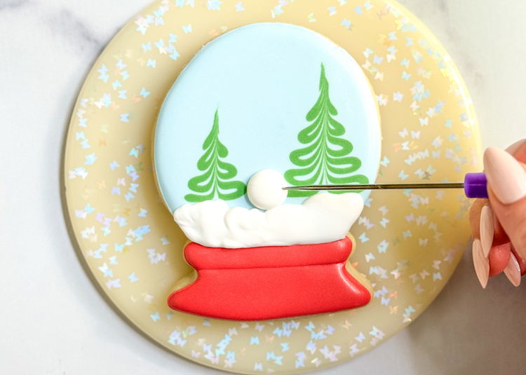 Image of We will now be piping a snowman in between the trees. Using the white outline consistency icing, pipe a large dot, which be the body of the snowman. Smooth out the icing, if needed, with a scribe tool or toothpick. Let this icing crust over for 10-15 minutes before moving onto the next step. 