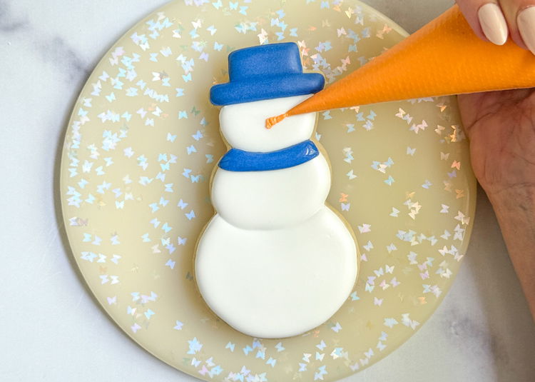 Image of Pipe the snowman’s “carrot nose” with the orange outline consistency icing. 