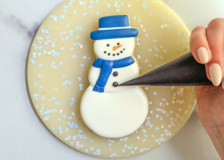 Image of Using the black outline consistency icing, pipe two black dots on the snowman’s body. Sit back and admire your charming snowman cookie! 