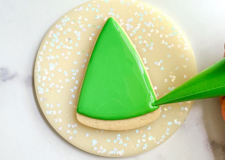 Image of Fill in the shape of the tree with the light green flood consistency icing. Use your scribe tool or a toothpick to smooth out the icing and pop any air bubbles that come up. Allow this section to dry for 20-30 minutes or until the icing just starts to crust over before moving onto the next step.