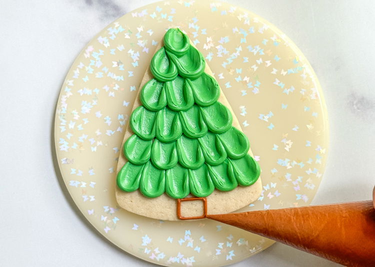 Image of Using the brown outline consistency icing, pipe a small square at the bottom of the tree. 