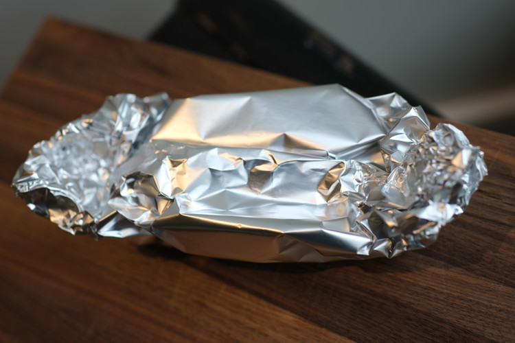 Image of wrap garlic in tin foil. drizzle with extra virgin olive oil. Create a foil pouch for garlic leaving a bit of an air pocket above the cut side of the garlic (so garlic does not stick to foil).