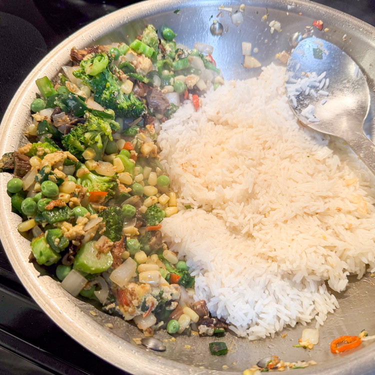 Image of Make a well again or remove the stuff from the skillet since we all want some crispy rice. Add ¼ cup vegetable oil to the bottom of that hot pan and add in all the rice. Press until it is...