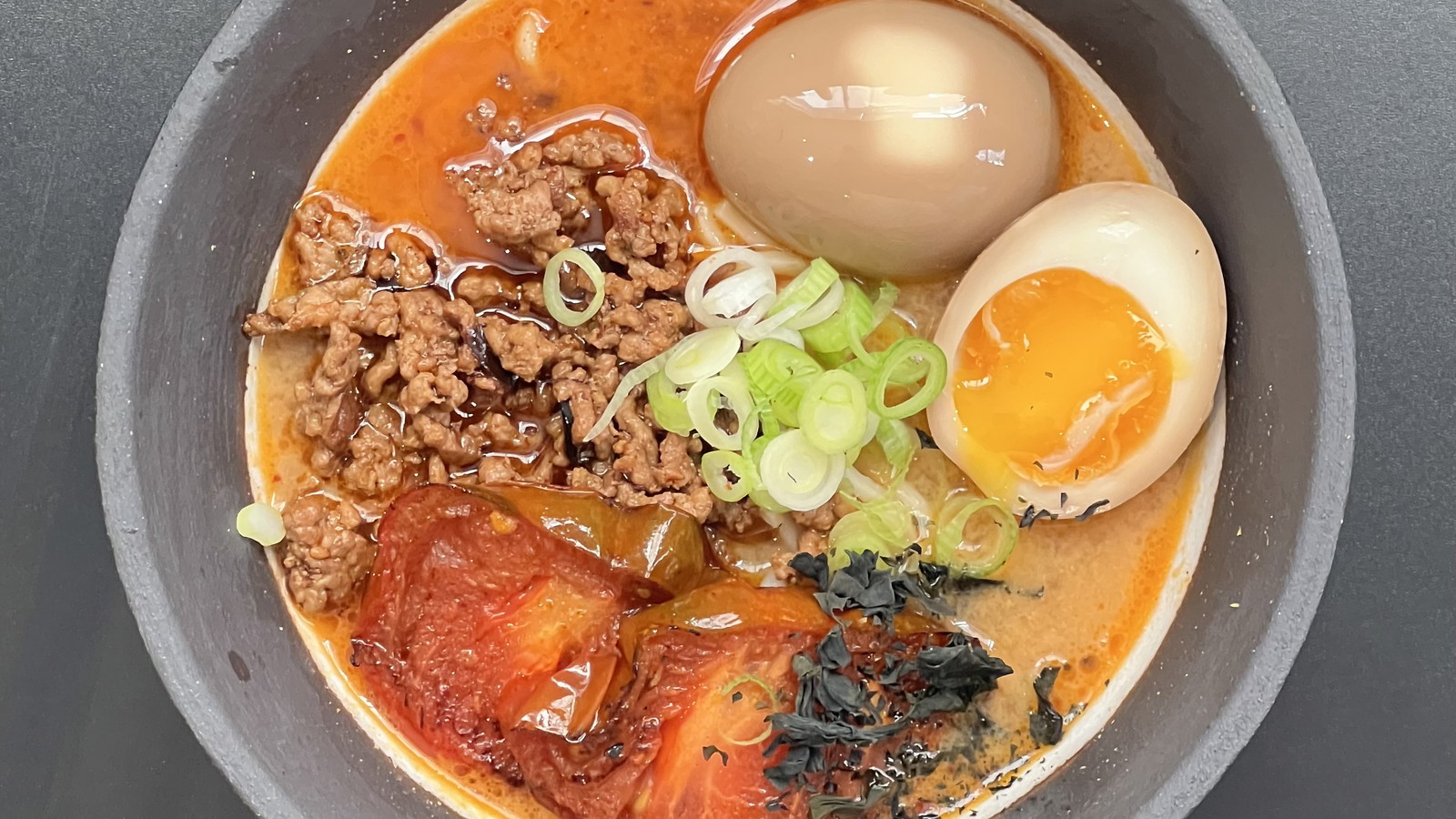 Schüssel mit TADA Ramen, voller würzigem Tantan-Geschmack, saftigem Hackfleisch, geschmorten Tomaten, frischen Frühlingszwiebeln und einem perfekt marinierten Ei in einer aromatischen, leicht scharfen Brühe.