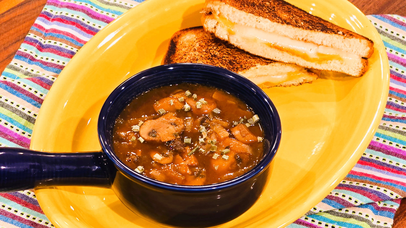 Image of a mushroom and onion soup with a grilled cheese sandwich on the side.