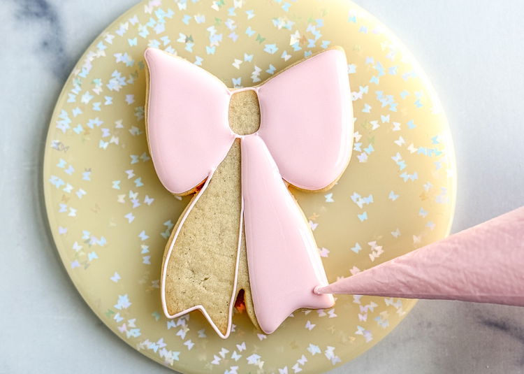 Image of Using the light pink flood icing, fill in the bottom right section of the bow. Use your scribe tool or a toothpick to smooth out the icing and pop any air bubbles that come up.  Allow this section to dry for 20-30 minutes before moving onto the next step. 