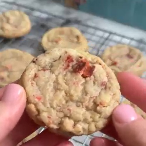 Strawberry sugar cookie held over a batch of freshly baked cookies.