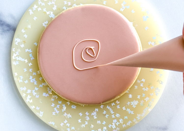 Image of Using the light brown outline consistency icing, start piping the nest onto your circle shape. Starting from the inside of the circle moving out, make uneven concentric circles and continue circling the outer edge, building height around the edge of the cookie shape.  Pro Tip: Ensure your icing consistency is thick enough to achieve this design. If your lines are blurring into each other, you can thicken up your icing with some additional powdered sugar until the desired consistency is achieved.  Allow this icing to dry for at least 1 hour or until firm before adding the royal icing egg transfers. 