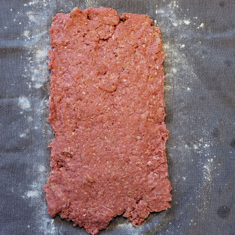 Image of Ein Küchentuch leicht mit Mehl bestäuben. Hackfleisch darauf geben und...