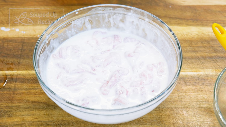 Image of In a separate bowl, mix the cornstarch with the water until it becomes a smooth, thick batter. Then combine the marinated pork with the batter and mix until the meat is coated nicely.