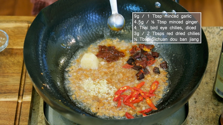 Image of Add a drizzle of Chinese cooking wine and stir to deglaze the bottom. Add the minced garlic, ginger, Thai bird eye chilies, red dried chilies, and ½ Tbsp of Dou Ban Jiang.