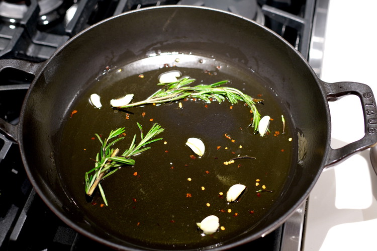 Image of Add olive oil, rosemary spring, red pepper and crushed garlic to the pan and cook herbs in oil for about 4 minutes.  Stir to prevent burning—you are infusing the oil with the herb flavors