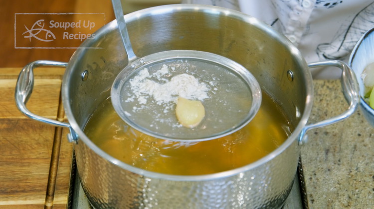 Image of We are going to use the chicken cooking broth to make a delicious hearty soup. Remove the soggy aromatics and sieve out the impurities.