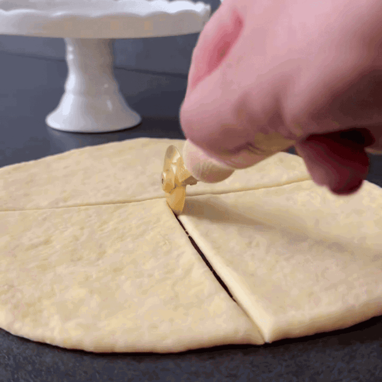 Image of Avant de garnir, étirez doucement chaque triangle légèrement dans le sens de la longueur et de la largeur avec vos mains ou un petit rouleau pour agrandir la forme et rendre les petits pains plus aérés.