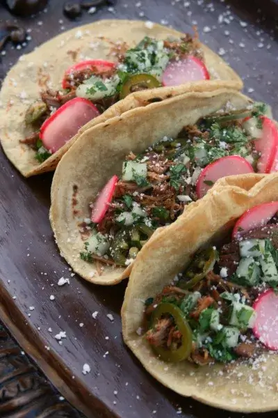 Image of To assemble, use 2 tortillas per taco (to prevent them from falling apart) and fill each taco with shredded pork, chopped cilantro/onion, pickled jalapenos/radishes, and sprinkle with cotija cheese.