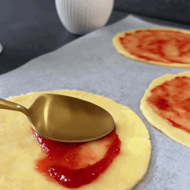 Image of Eine dünne Schicht Erdbeermarmelade gleichmäßig auf jeden Teigkreis streichen, dabei einen kleinen Rand um die Ränder lassen.