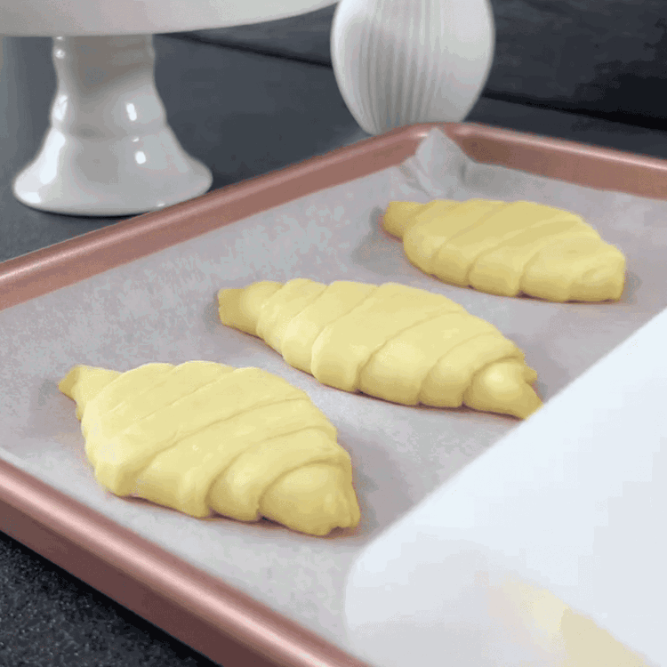 Image of Coloca otra hoja de papel pergamino encima de los croissants y coloca una segunda bandeja para hornear del mismo tamaño encima, presionando ligeramente para aplanar los croissants. Opcionalmente, añade peso encima para asegurarte de que se mantengan planos.