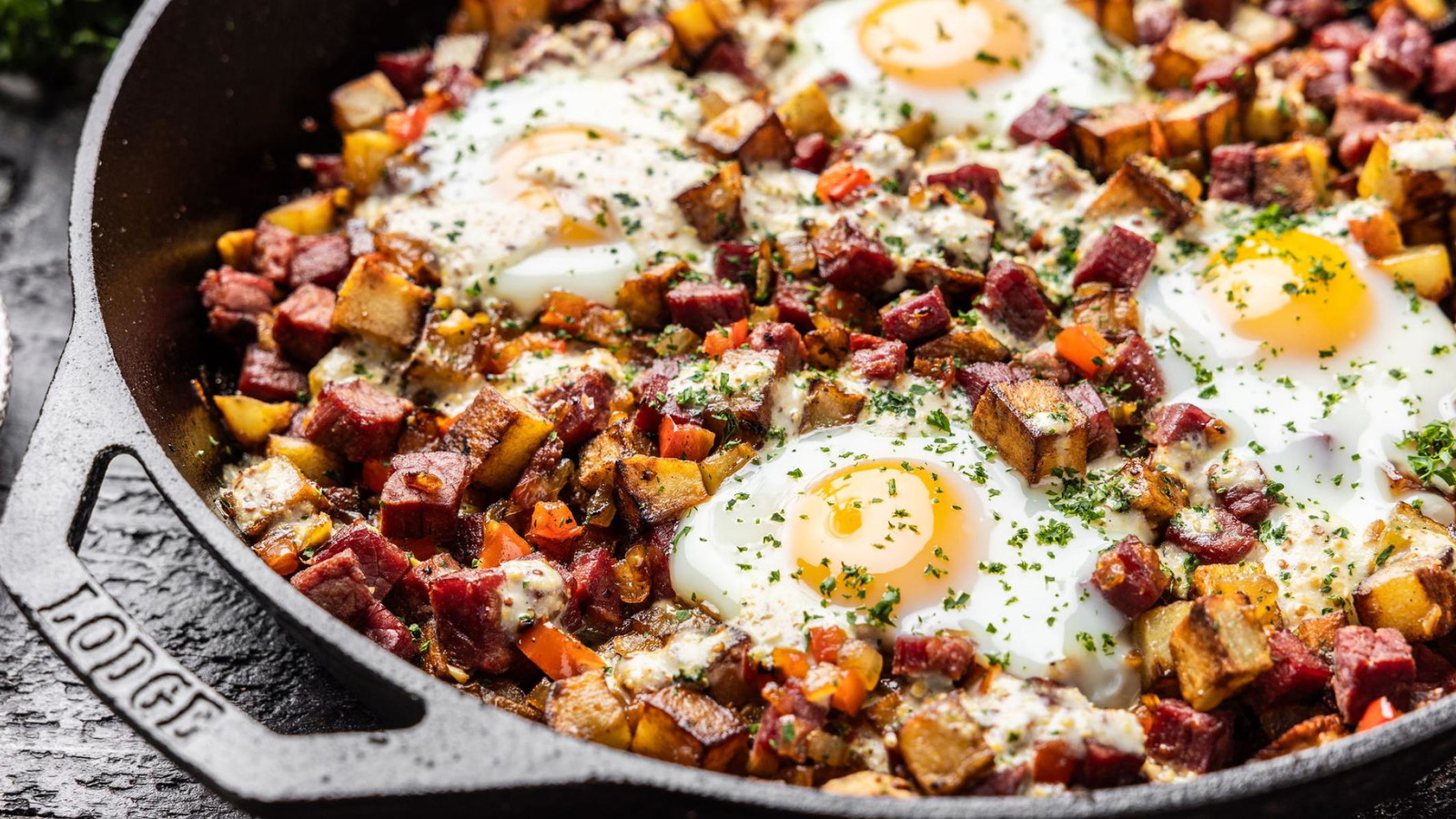 A cast iron skillet with four eggs resting atop the corned beef hash, ready to be served