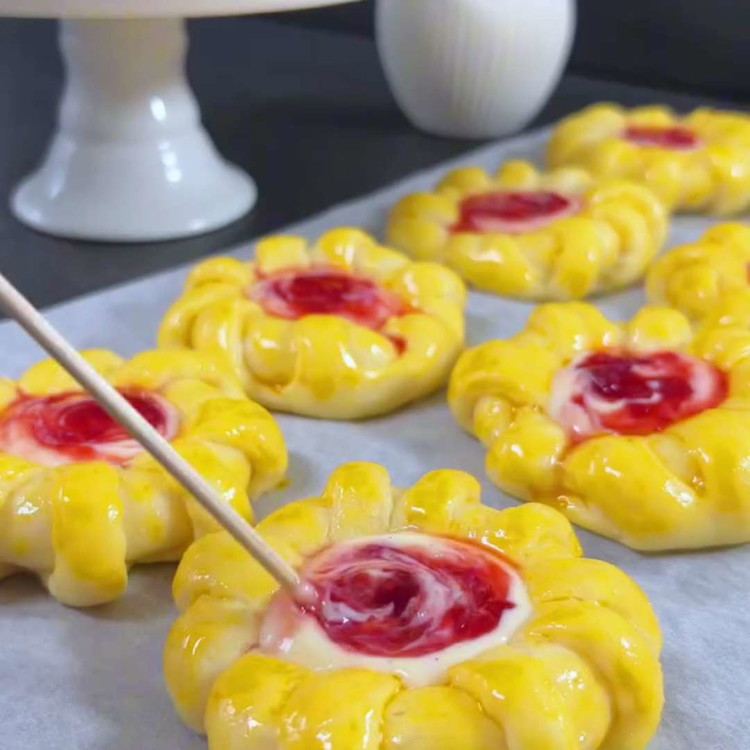 Image of Allarga il cerchio interno di ogni cerchio di impasto con le dita e riempi con la miscela di quark. Aggiungi un cucchiaino di marmellata di fragole sopra.