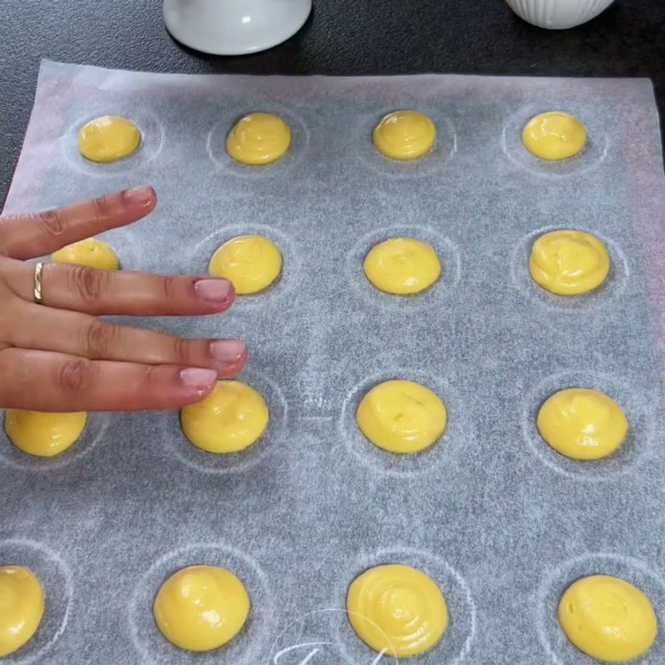 Image of Riempi una sac à poche con l'impasto. Forma piccole porzioni di impasto con un diametro di 3 cm su una teglia rivestita di carta da forno. Spennella con uovo e cospargi di zucchero perlato.