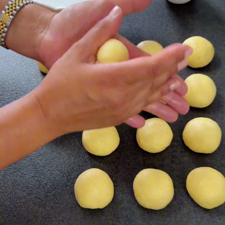 Image of Despeje a massa em uma superfície levemente enfarinhada e divida em cerca de 15 pedaços iguais. Modele cada pedaço em uma bola e coloque-os em uma assadeira forrada com papel manteiga. Achate levemente as bolas. Cubra-as e deixe crescer novamente...