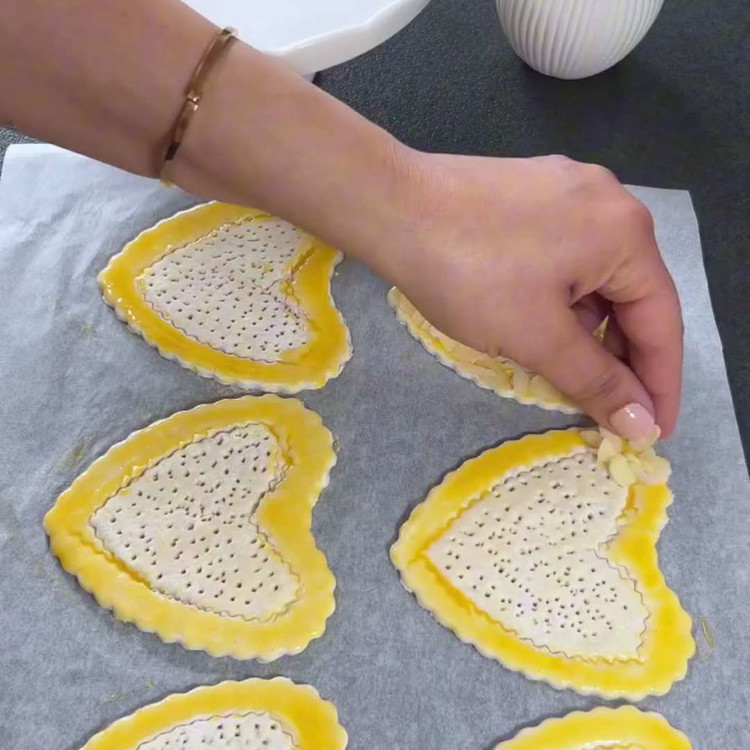 Image of Kalplerin kenarlarını yumurta sarısı ve krema karışımı ile fırçalayın, ardından üzerlerine dilimlenmiş badem serpin.