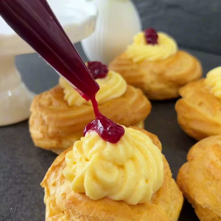 Image of Taglia con attenzione a metà le zeppole raffreddate con un coltello piccolo. Riempi una sac à poche con un beccuccio piccolo con il ripieno e farcisci la metà inferiore delle zeppole. Posiziona la metà superiore sopra.