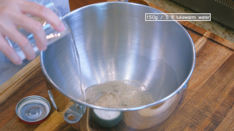 Image of In a stand mixer bowl, thoroughly stir the yeast with the lukewarm water and wait for 5 minutes to allow the yeast to wake up.