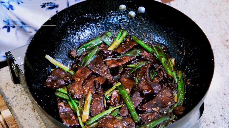 Image of Introduce the beef back into the wok, toss in the green part of the scallion stalks, and mix until the beef is well-coated.
