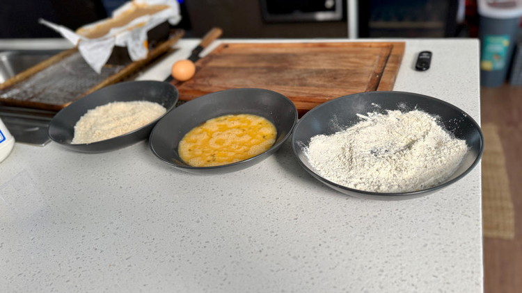 Image of set up 3x plates or bowls. First with flour and italian herbs. Second with beaten eggs and sriracha sauce. Third with panko breadcrumbs.