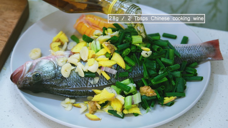 Image of Add the diced ginger, garlic, scallions, Chinese cooking wine, and the fish to a big mixing bowl and rub the aromatics onto the fish surface for a few minutes. Let the fish rest at room temperature for 20 minutes.
