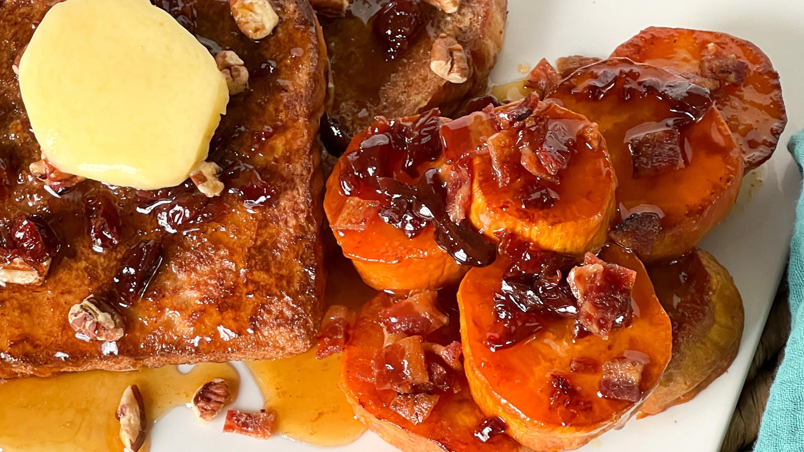 A pile of roasted sweet potatoes topped with crispy bacon and dried cherries, dripping with maple syrup