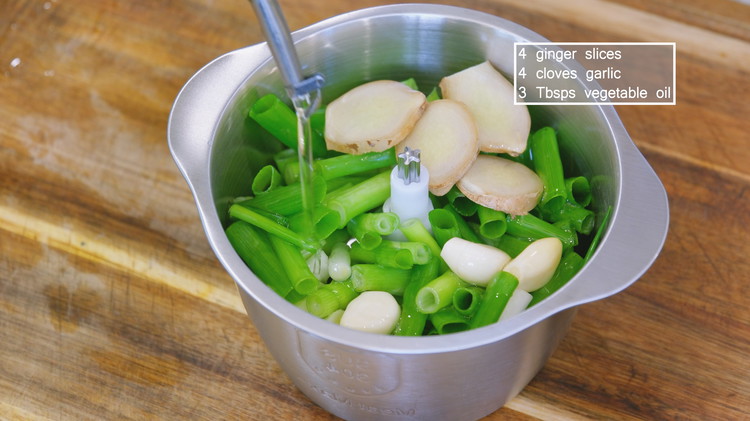 Image of Add the scallions, ginger slices, garlic cloves, and 3 tbsp of oil to a food processor and blend into a fine paste.
