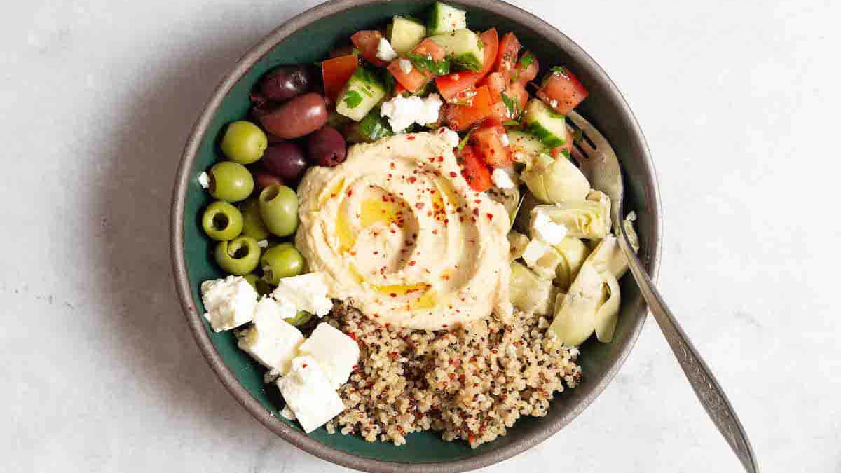 an overhead photo of a mediterranean bowl with quinoa with a fork in it.