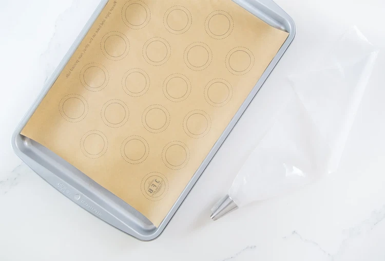 Image of Separate eggs. Place whites in a glass or metal bowl (not plastic) and let come to room temperature. Save yolks for another use. Line baking sheets with parchment paper, printed side down. Fit piping tip into bag.