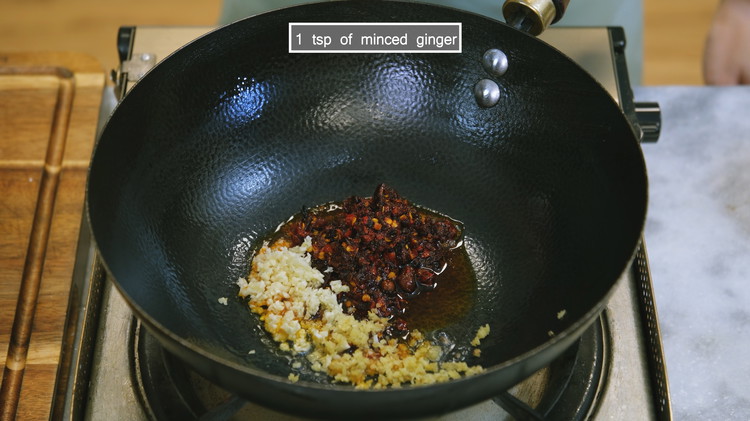 Image of To make the General Tso's sauce, add 2.5 Tbsps of Lao Gan Ma Chili Crisp, 2 tsp of minced garlic and 1 tsp of minced ginger to a wok. Saute over low heat until fragrant.