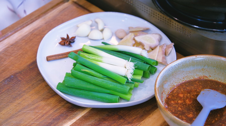 Image of While the pork is draining, prepare the garlic cloves, ginger slices, scallion stalks, star anise, and cinnamon stick. Having these ingredients beforehand avoids rummaging around while caramelizing the sugar.