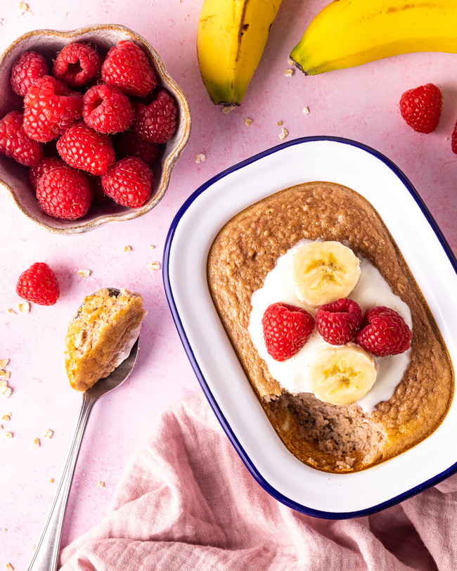 A bowl of fresh raspberries laid next to a tray of baked Oats