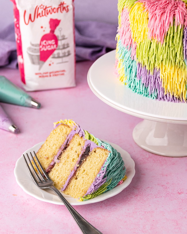 A shaggy cake iced using the grass piping nozzle to create a funky retro effect. A slice has been cut showing a jam and buttercream layer in between sponge layers.
