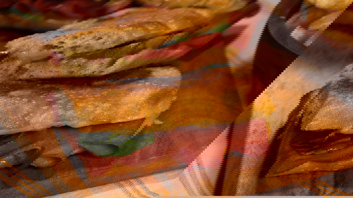 Golden -brown toasted paninis with slices of Halal bologna, spinach, and melted cheese, served on a wood serving board.